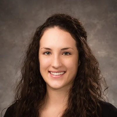 Chiropractor Ellie Ryan Smiling In Black Top On Grey Background