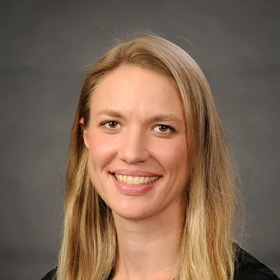Chiropractor Emily Doudlah Smiling In Front Of Grey Background