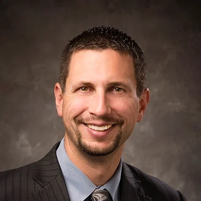 Chiropractor Jason Mackey Smiling In Striped Suit And Blue Shirt