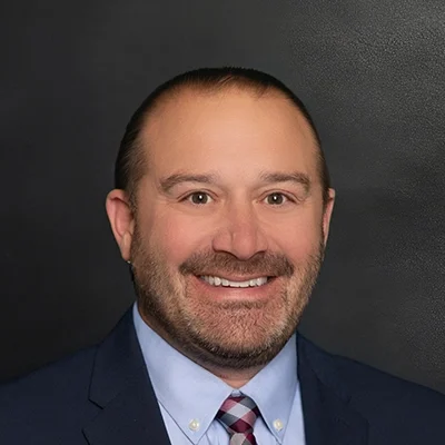 Chiropractor Benjamin Mikla Smiling In Front Of Black Wall