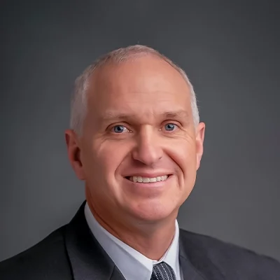 Chiropractor Nathan Considine Smiling In Grey Suit And Grey Tie