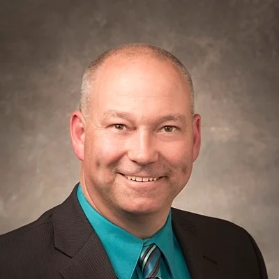 Chiropractor Sauk City WI Randall Hohenstein About Chiropractor Randall Hohenstein Smiling In Grey Suit And Turquoise Shirt