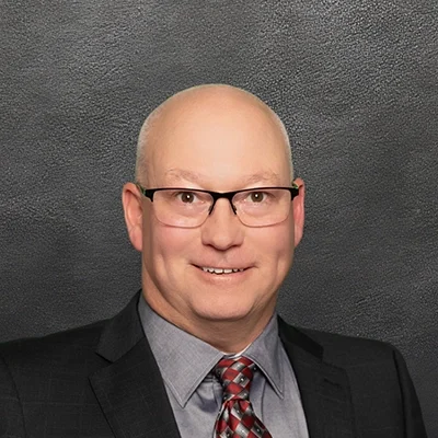 Chiropractor Randall Hohenstein Smiling In Front Of Black Wall