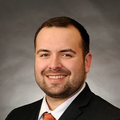 Chiropractor Andrew Holzli Smiling In Black Suit With Orange Tie