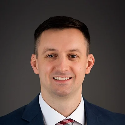 Chiropractor Jason Ballweg Smiling In Navy Suit With Plaid Tie