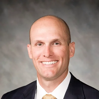 Chiropractor Brett Hoeft Smiling In Dark Grey Suit and Yellow Tie