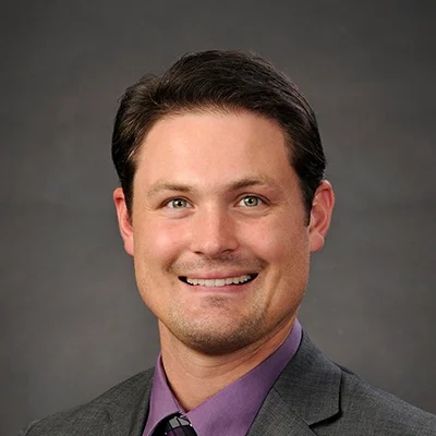 Chiropractor Logan Clarahan Smiling In Grey Suit With Purple Shirt