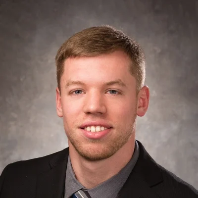 Chiropractor Ryan Weyenberg Smiling In Black Suit With Grey Shirt